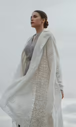 woman standing in front of the camera wearing a white coat and floral shirt dress