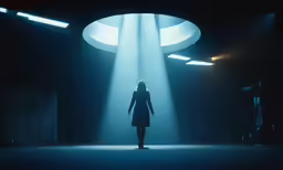 a woman standing in the dark while light shines down on her