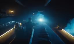two people looking at their cellphones while a train drives in the dark