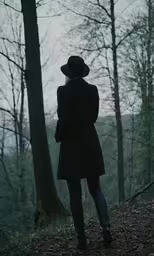 woman standing alone in the forest facing away from the camera
