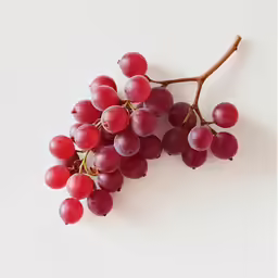 a bunch of red grapes hang from a stick