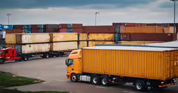 freight trucks parked in front of large containers on the street,a yellow semi truck next to lots of cargo trucks