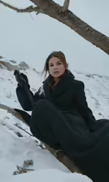 a woman sitting in the snow next to a tree