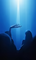 a dark photo with one person reaching up to the sky