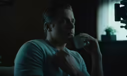 a man sitting in front of a camera drinking out of a cup