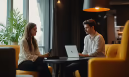 two people sitting at a table looking at a laptop