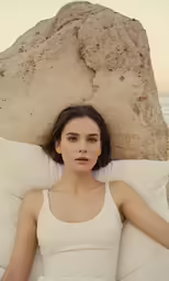 a woman lying on a large rock next to the ocean