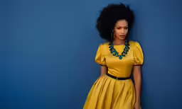 a woman in yellow is posing against a blue wall