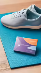 a pair of sneakers sits on a bright colored mat beside a business card