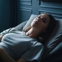 a woman sleeping on a grey bed with her eyes closed