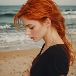 a red headed woman stands on the beach looking at her cell phone