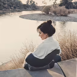 a young woman sitting on top of a cement wall near a river