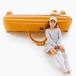 the little girl is sitting near an orange bag