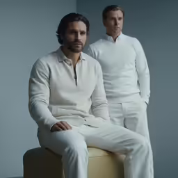 a pair of men in white linens and slacks sit on a stool