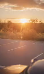 a car is parked in a parking lot with the sun rising