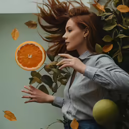a woman throwing oranges into the air next to leaves and a plant