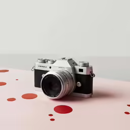 a black and silver camera on pink with confetti