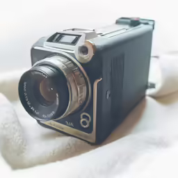 a photo camera sitting on top of a bed next to a white sheet