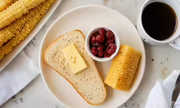 a piece of bread and a bowl of berries and butter with some corn on the cob