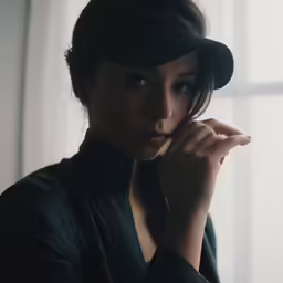 a young lady wearing a baseball hat stands in front of the window