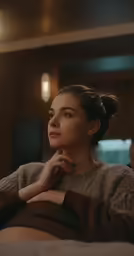 a woman sits on a bed wearing a sweater