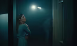 a woman is looking out a window at someone standing in the dark