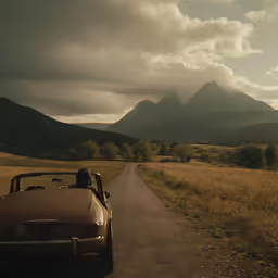 an old convertible car is traveling down the road into a beautiful landscape