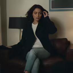 a woman in white shirt and black jacket sitting on leather couch