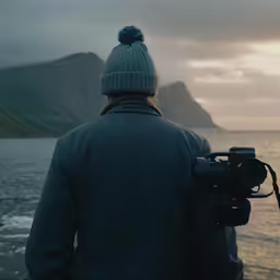 a man with a camera and standing next to a body of water