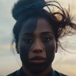 a woman with her hair blown by wind in a darkened landscape