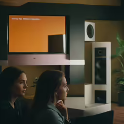 two women are talking near a stereo and speakers