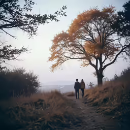 two people walking together on a trail surrounded by trees