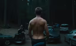 a shirtless man walking in front of parked cars