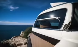 the sun shines brightly in the background as cars drive on a cliff overlooking the ocean