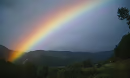 a very bright rainbow appears over a mountain range
