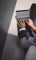 a person is sitting with his laptop on the ground