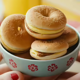 someone holding up a bowl with a plate of hamburgers and bagels