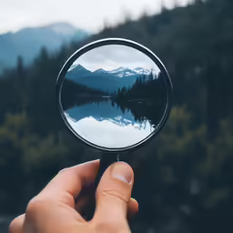 someone holding a magnifying glass reflecting mountains in the water