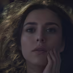an attractive woman with curly hair looking down in the dark