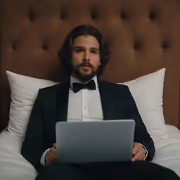 a man sitting on a bed with a laptop in his lap
