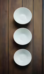 three white bowls sitting on top of wooden table