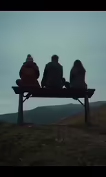 three people are sitting on a bench in the mountain