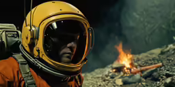 a person in a helmet and jacket in front of a fire