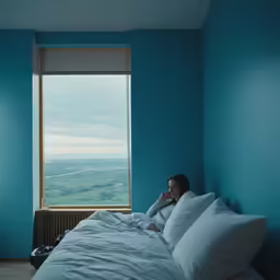 the young lady sits on the bed looking out a window