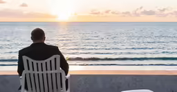 there is a man sitting on the bench near the beach