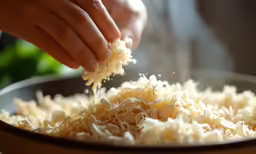 a man is sprinkling shredded cheese into a frying pan