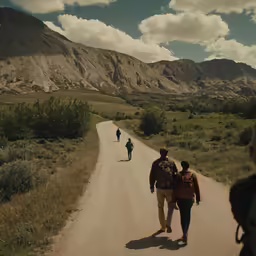 people walking down a dirt road with mountains in the background