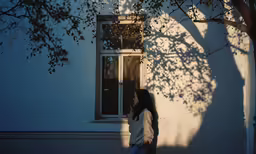 a woman standing by a window while looking at a tree