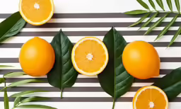 some oranges sitting on top of leaves and striped table cloth