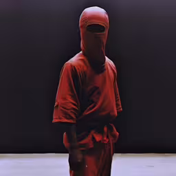 a person wearing red is standing with his face covered,a person in red is standing outside